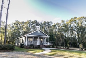 Small blue gray mobile home with a front and side porch with white railing.
